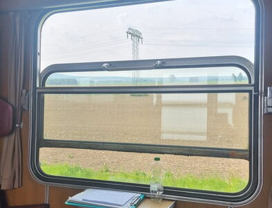 Blick aus dem geöffneten Zugfenster auf Feldlandschaft und einem Strommast.